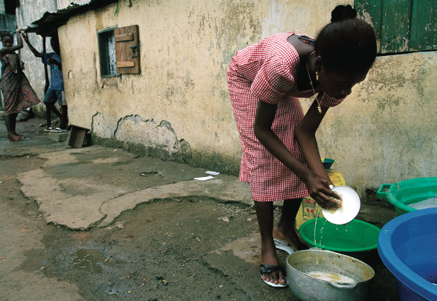 Une fille employée comme domestique fait la vaisselle pour sa famille d’accueil, avant d’aller à l’école primaire à Conakry. © 2007 Susan Meiselas/Magnun Photos